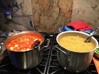 Vegetable soup and curried squash soup in stainless steel pots on a gas stove.