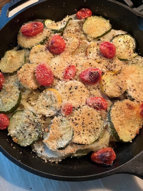 Potato zucchini bake with tomatoes in a cast iron skillet.