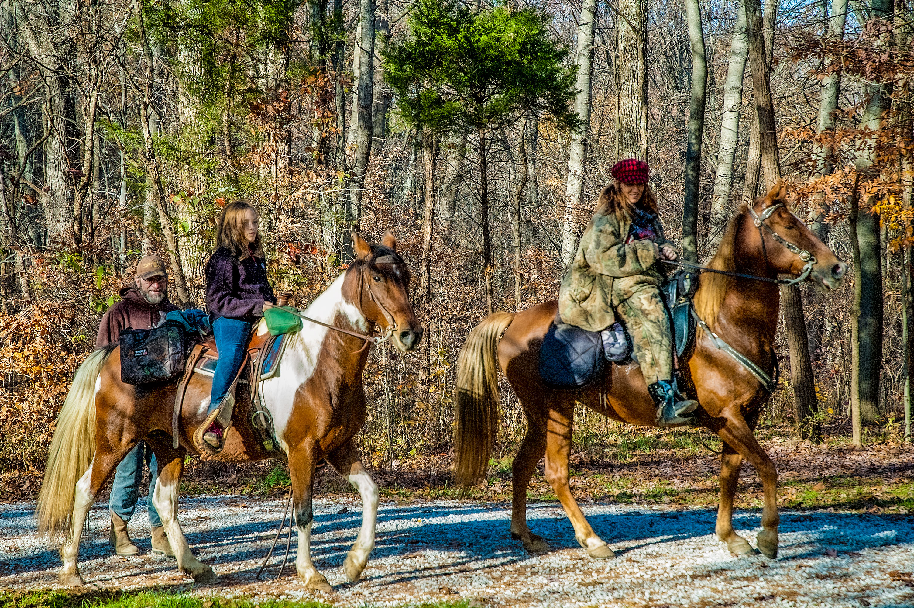 A woman and a girl ride horses on a trail in the Hoosier National Forest as a man stands by offering assistance.