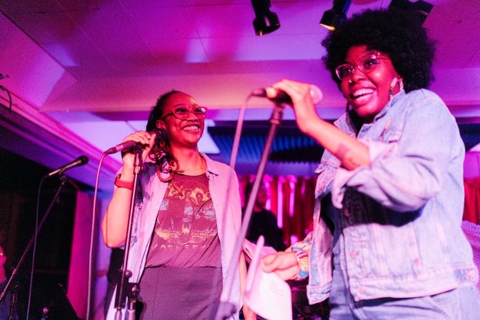Olivia Ekeh (l) and Nia I'man Smith (r) smile on stage while holding microphones.