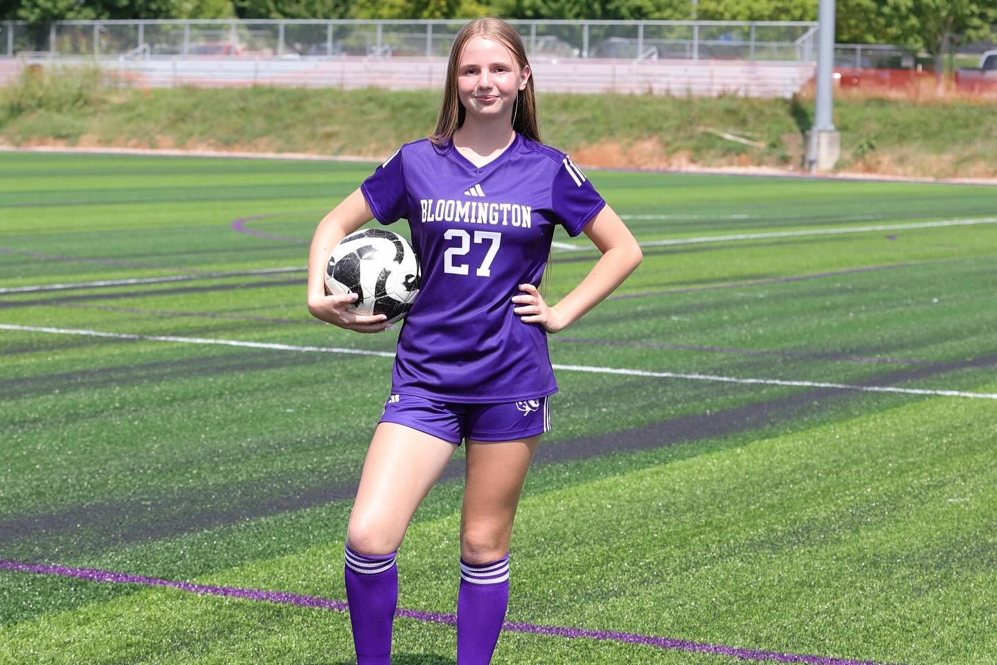 Charlotte Melick wears her purple Bloomington South soccer jersey and poses with a soccer ball.