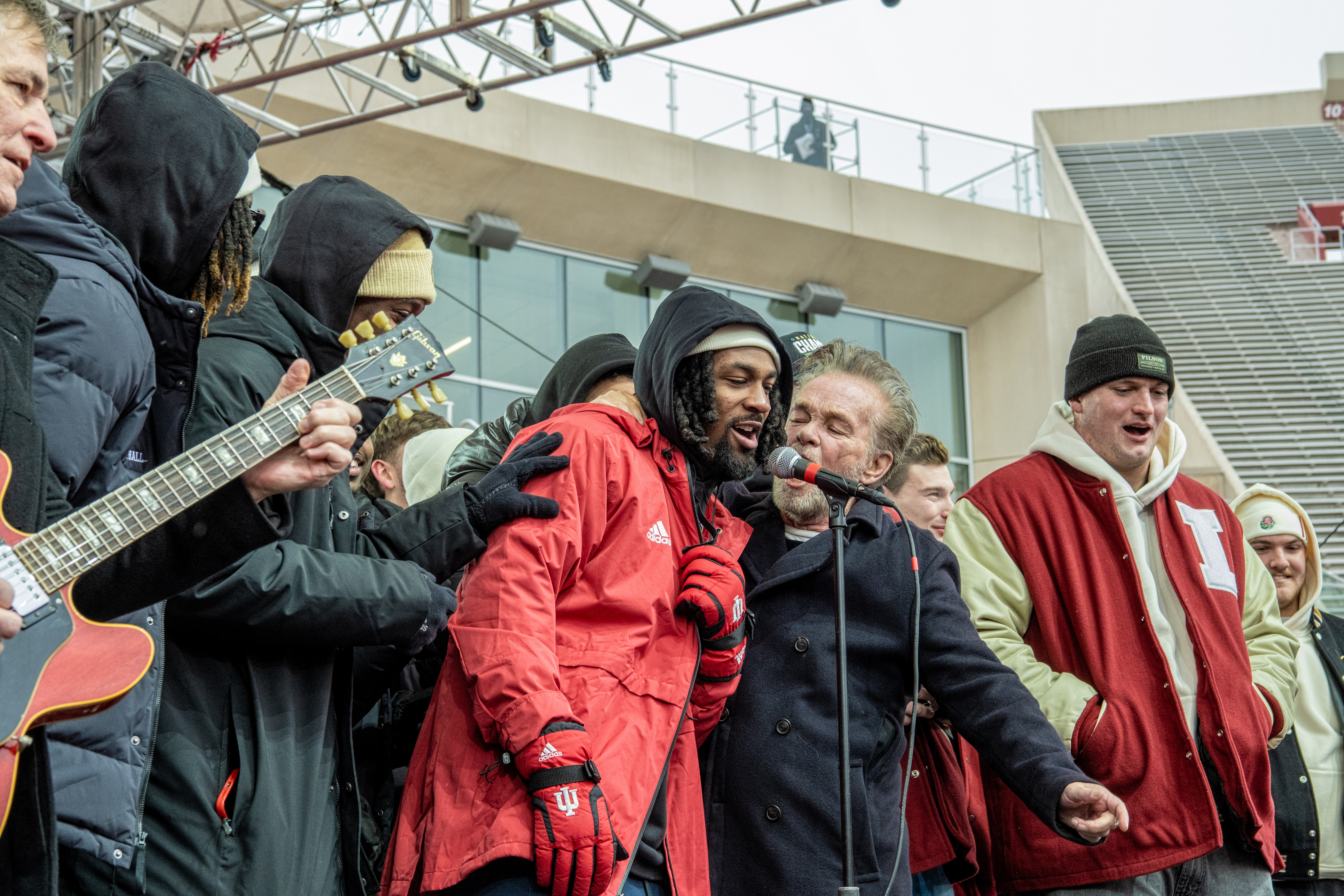 John Mellencamp sings his 1982 hit “Hurts So Good,” a sort of anthem for the team, while players Elijah Sarratt, Omar Cooper Jr., and Pat Coogan share the mic and sing along.