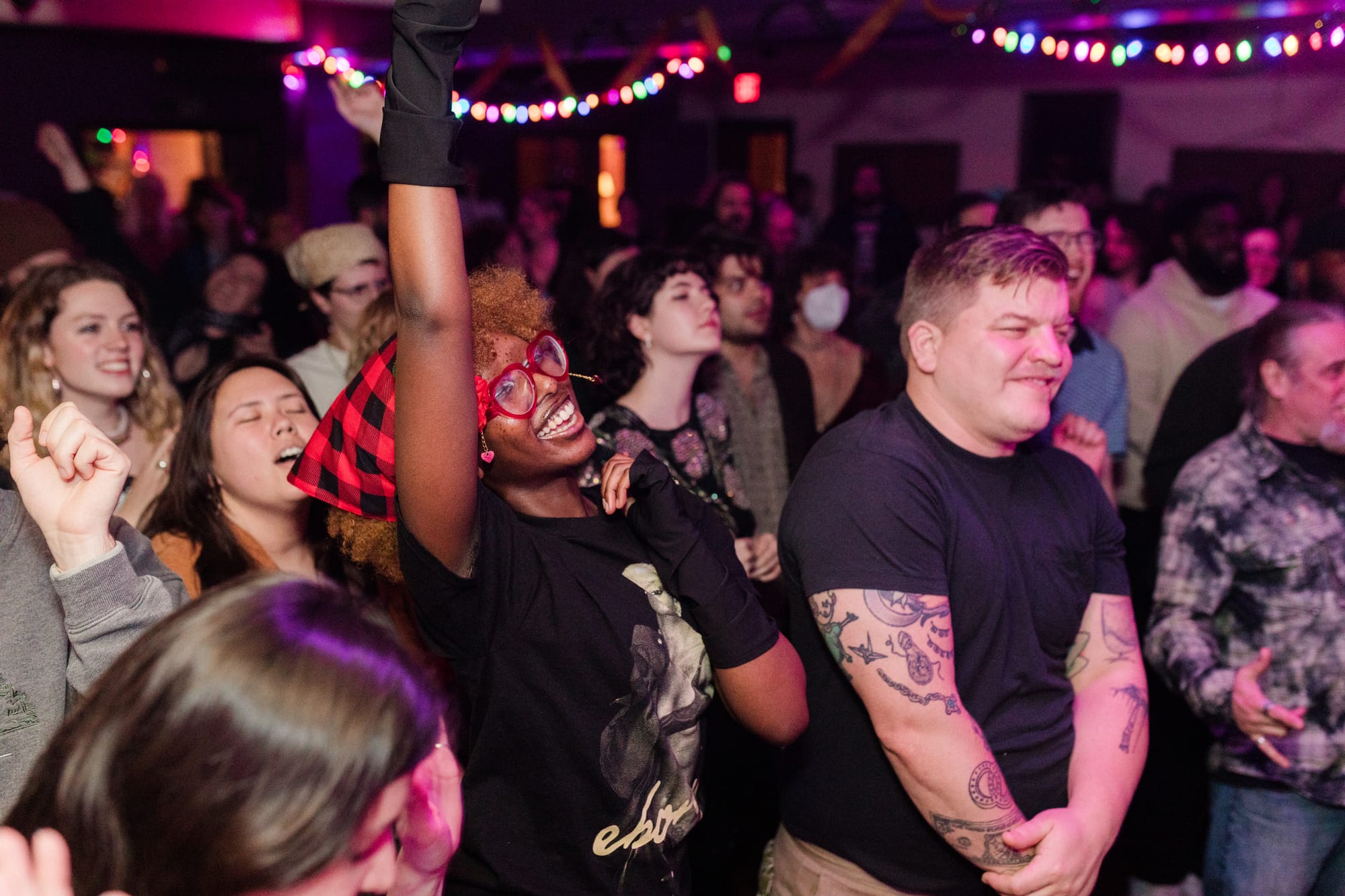 a crowd of smiling and dancing onlookers crowd into a basement music venue