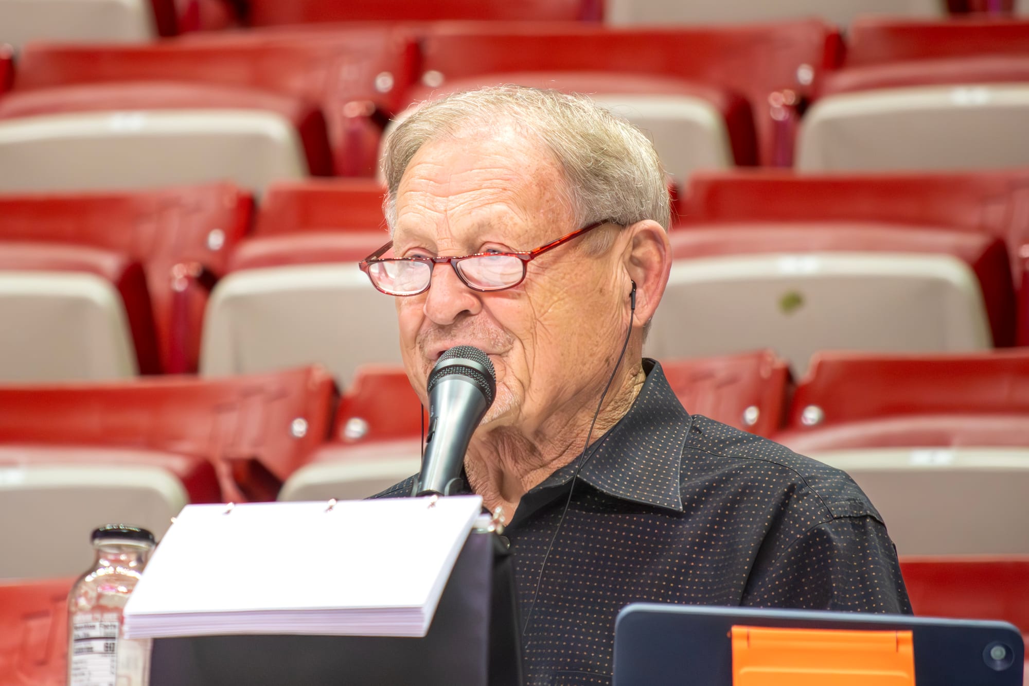 Don Fischer wearing red glasses and speaking into a microphone at Assembly Hall
