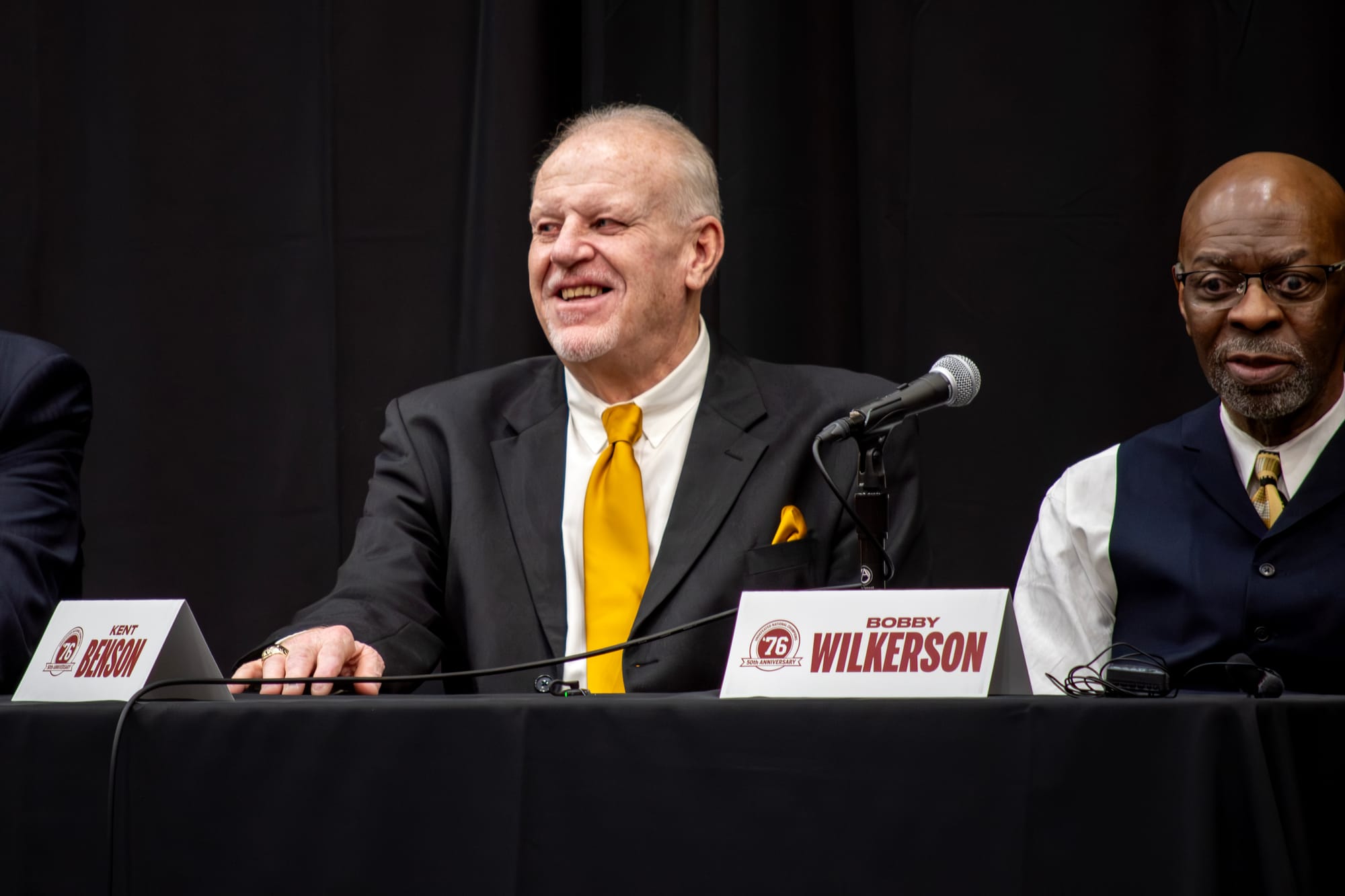 Kent Benson, a 71-year-old white man, wearing a black suit coat, white shirt, and yellow tie. Bobby Wilkerson, a 71-year-old black man, wears a blue suit vest over a white shirt.