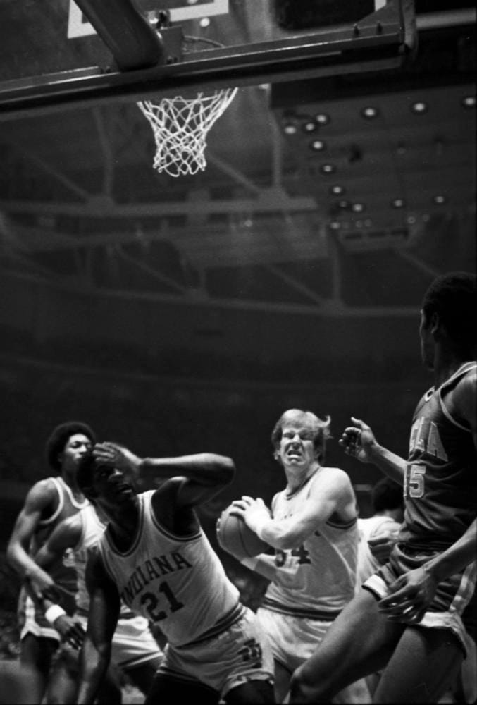 a black and white photo of college basketball players in close-quarters play under the net