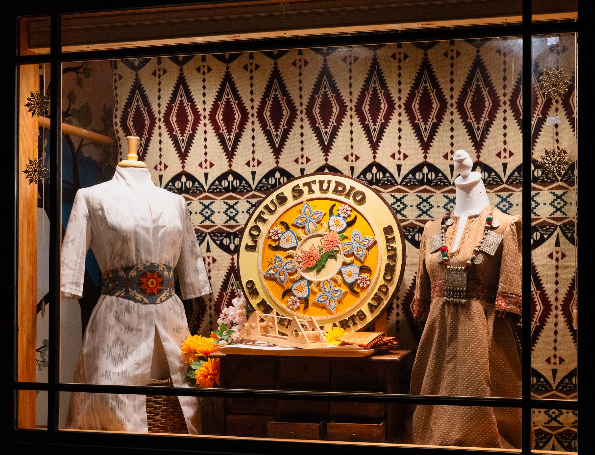 two hand-crafted garments on display in a store window. A sign with an embroidery motif reads "Lotus Studio"