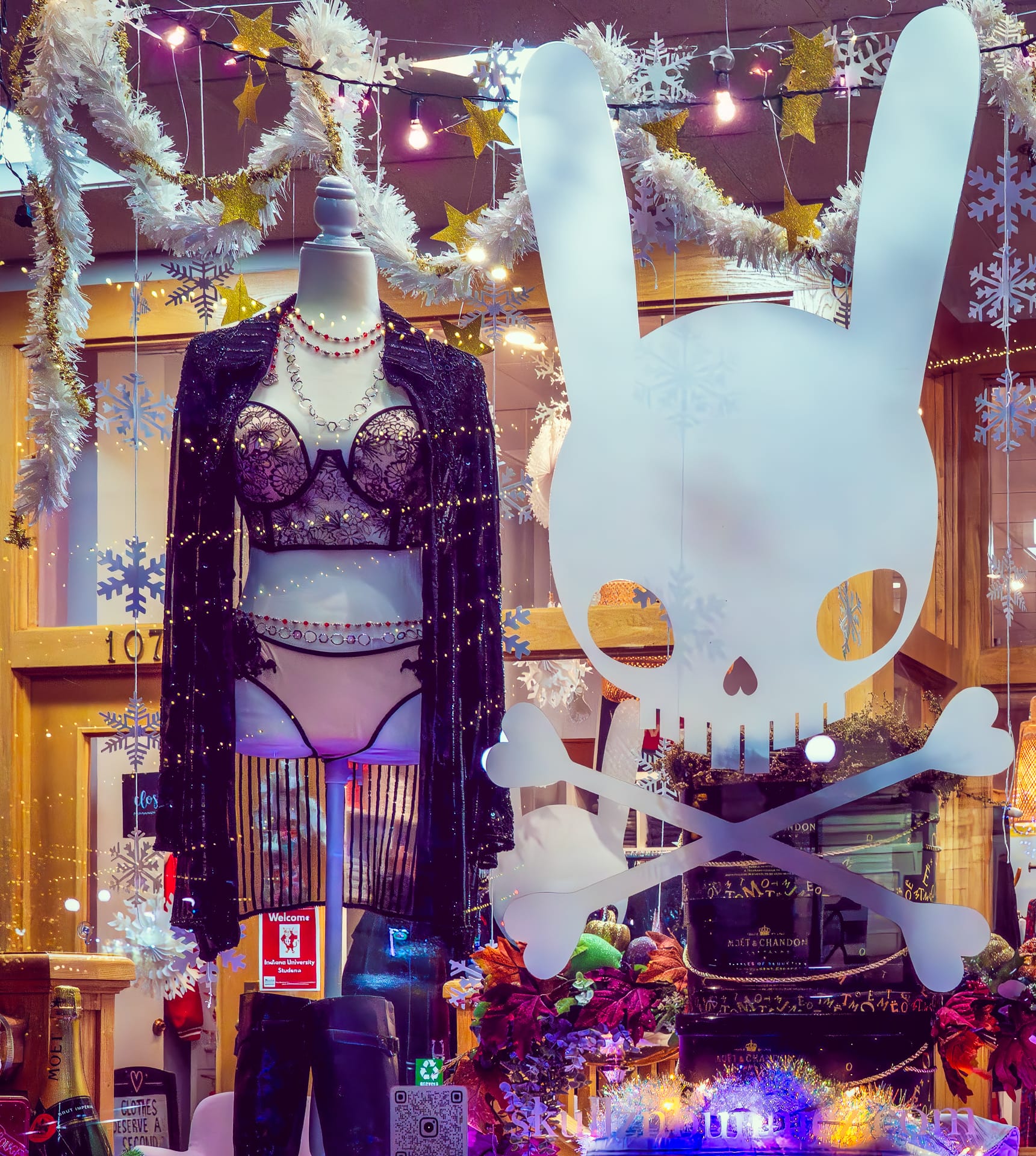 a mannequin wears a black and pink floral lingerie set in a store window display. Skullnbunniez's large "Bunny Skull and Crossbones" logo is adhered to the window