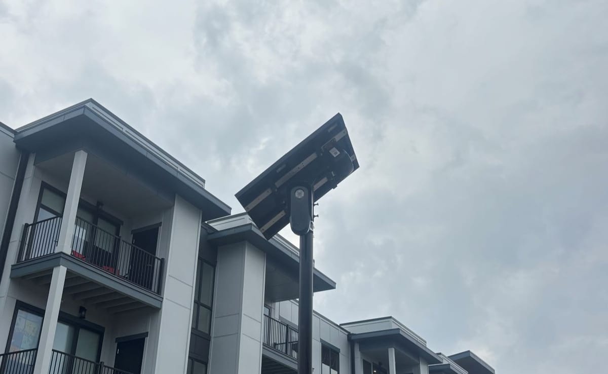 A black Flock security camera contrasts against a grey, cloudy sky