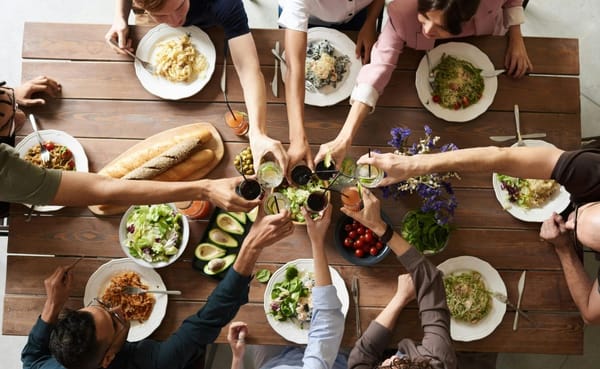 A group of people sit around a food-laden table, raising their glasses in a toast.