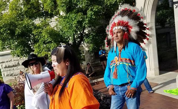 Writer Laura Reagan, wearing traditional Apache dress, speaks to a group of people at Sample Gates. As Halloween approaches,