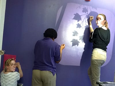 (l-r) Clements, a mentee, and Swank work on creating the "transitions wall" in Miss Ison's office. The wall helps Miss Ison track the needs of all students while they are in different stages of programming at MJCF. | Photo by Theresa Ochoa