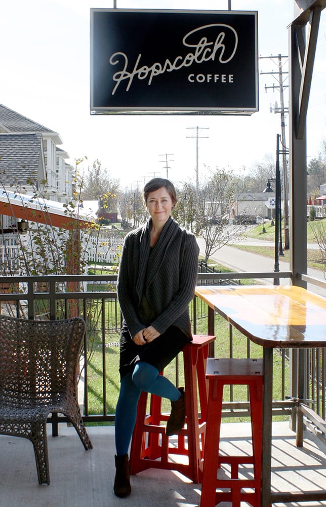 Jane Kupersmith, co-owner of Hopscotch Coffee, sits on the coffee shop's porch, which faces the B-Line Trail. Just down the B-Line is Cardinal Spirits, viewed on the right with its red umbrellas. | Photo by Jonna Mary Yost