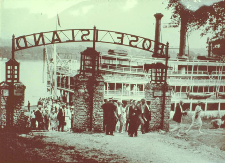 Rose Island historical photo from the Jeffersonville Public Library/Clark County Visual History; the caption reads: ‘The steamer, “America,” is shown embarking passengers at the entrance to Rose Island around 1925. Notice how well dressed everyone is. The park was used by many church, school and club groups which made the gatherings a social event and not just a day in the park.’